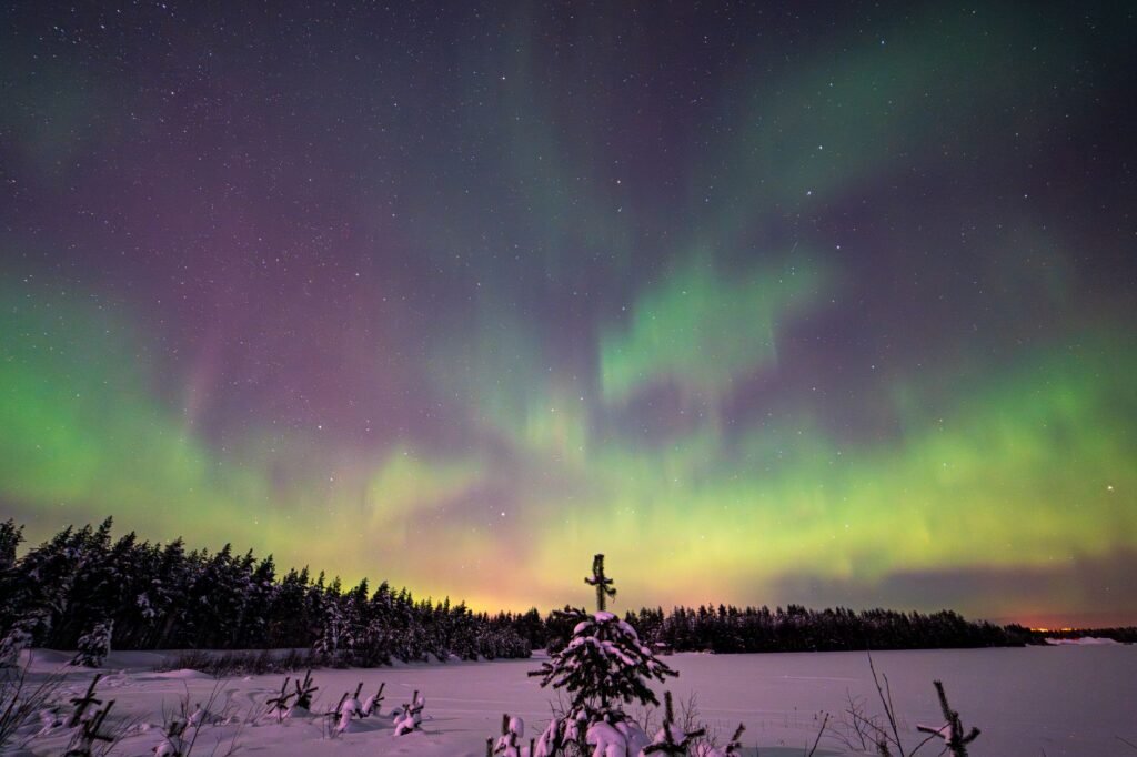 Lumoavat revontulet valaisevat talvisen yötaivaan seesteisen lumisen maiseman yllä Kemissä, Suomessa.