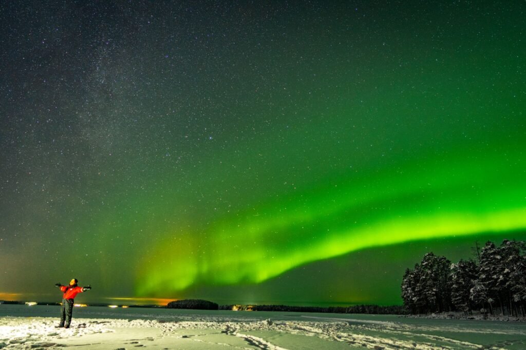 Revontulet valaisevat yötaivasta lumisen maiseman yllä Rovaniemissä, Suomessa.