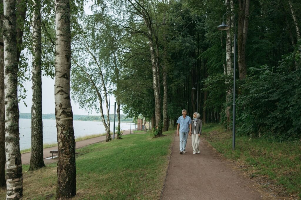 Vanha pariskunta nauttii rauhallisesta kävelystä puunreunustettua polkua pitkin rauhallisessa puistoympäristössä.