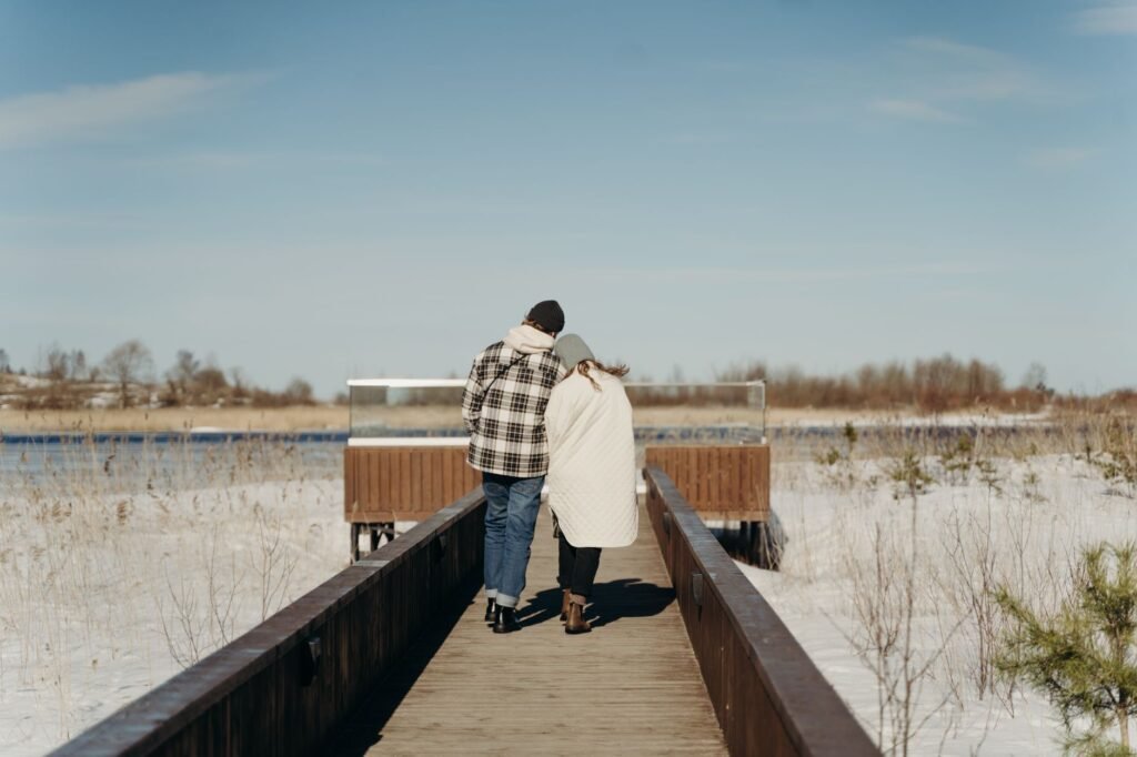 Pari kävelee lumisella laiturilla nauttien talvimaisemasta. Täydellinen romanttisiin ja kausiteemoihin.