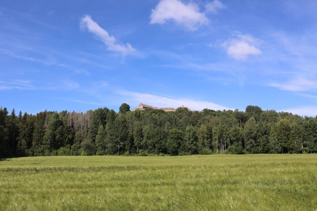 Rauhallinen maaseutu kaukaisine linnoineen, rehevine metsineen ja vihreine peltoineen kirkkaan sinisen taivaan alla.