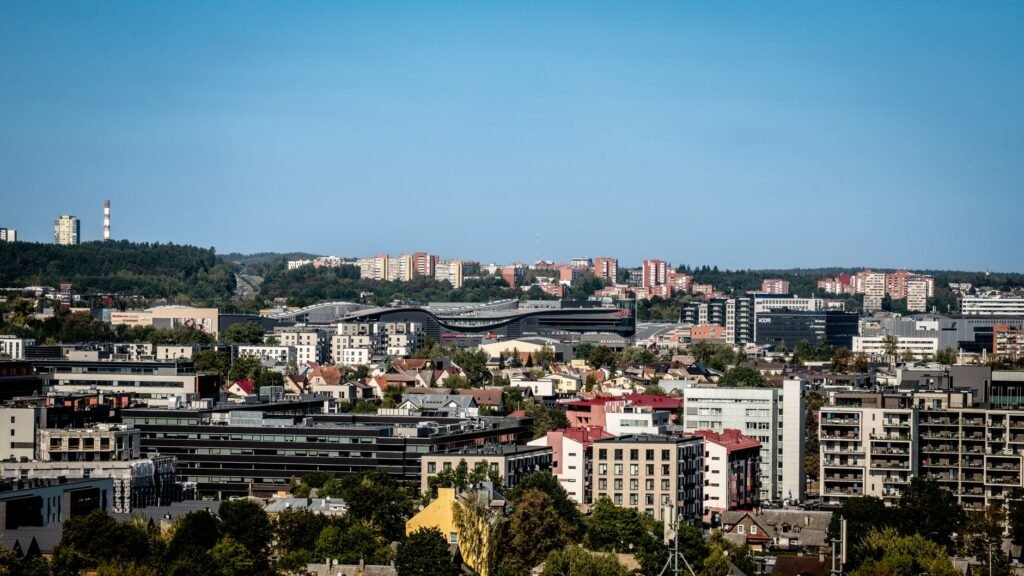 Panoraamanäkymä Vilnuksen horisontista, jossa on modernia ja historiallista arkkitehtuuria kirkkaan sinisen taivaan alla.