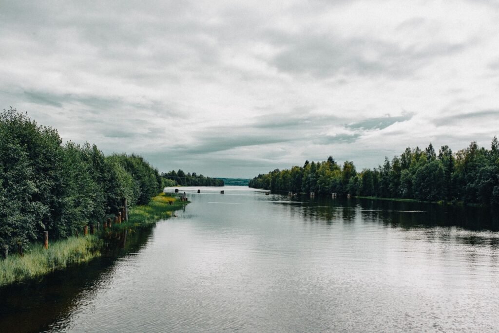 Rauhallinen jokimaisema vehreillä puilla ja pilvisellä taivaalla, täydellinen luonnon ystäville.