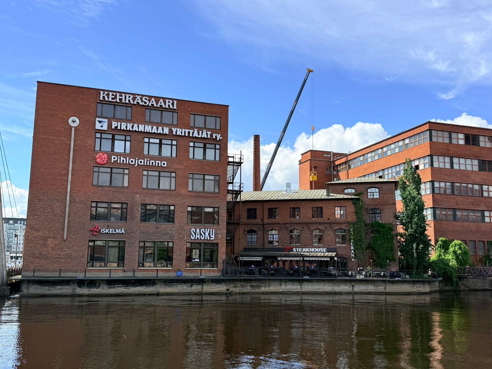 Rauhallinen jokivarsi Nokialla, taustalla vanhoja teollisuusrakennuksia