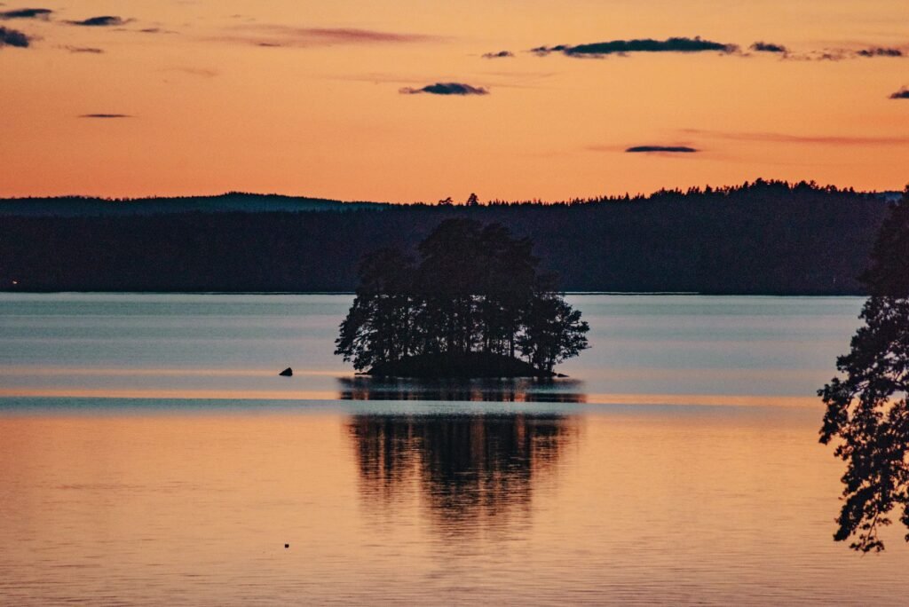 Rauhallinen saaren siluetti auringonlaskussa tyynellä järvivedellä.