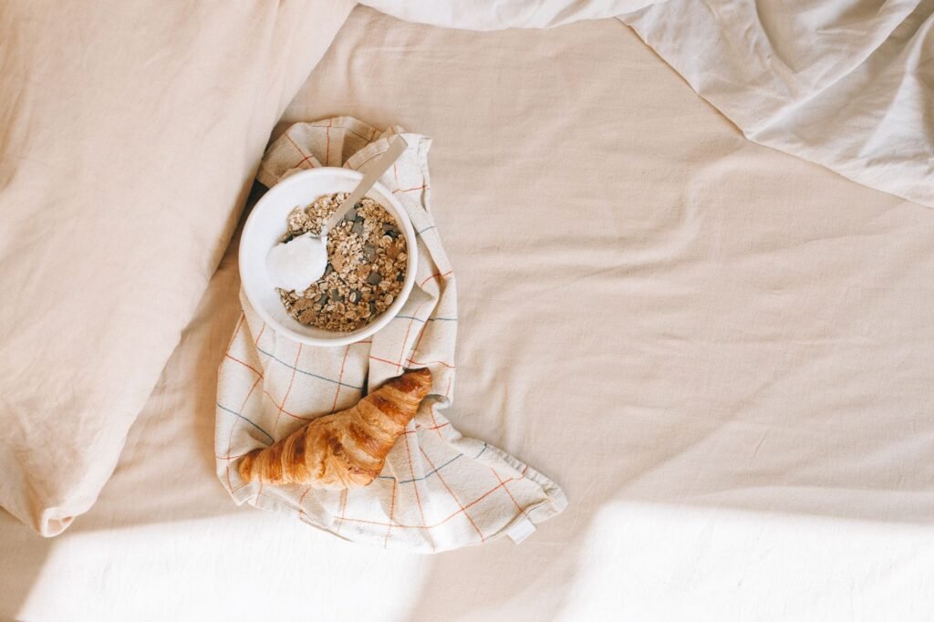 Mukava aamiainen, jossa on kulhollinen viljoja ja croissant sängyssä rentouttavaan aamuun.