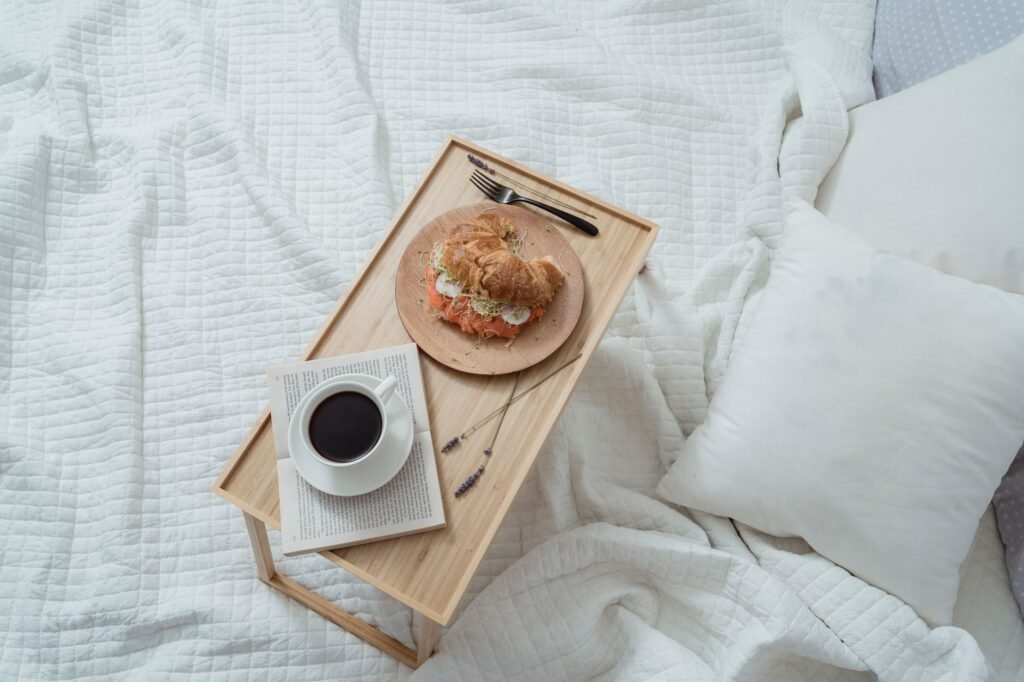Aamiainen sängyssä, jossa on croissant ja kahvia tarjottimella, huokuvana kodikasta mukavuutta.