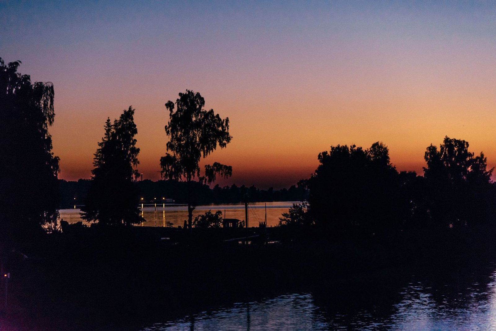 Rauhallinen ja tyyni auringonlasku Ladoga-järvellä Venäjällä, siluettimaisilla puilla värikkään taivaan edessä.