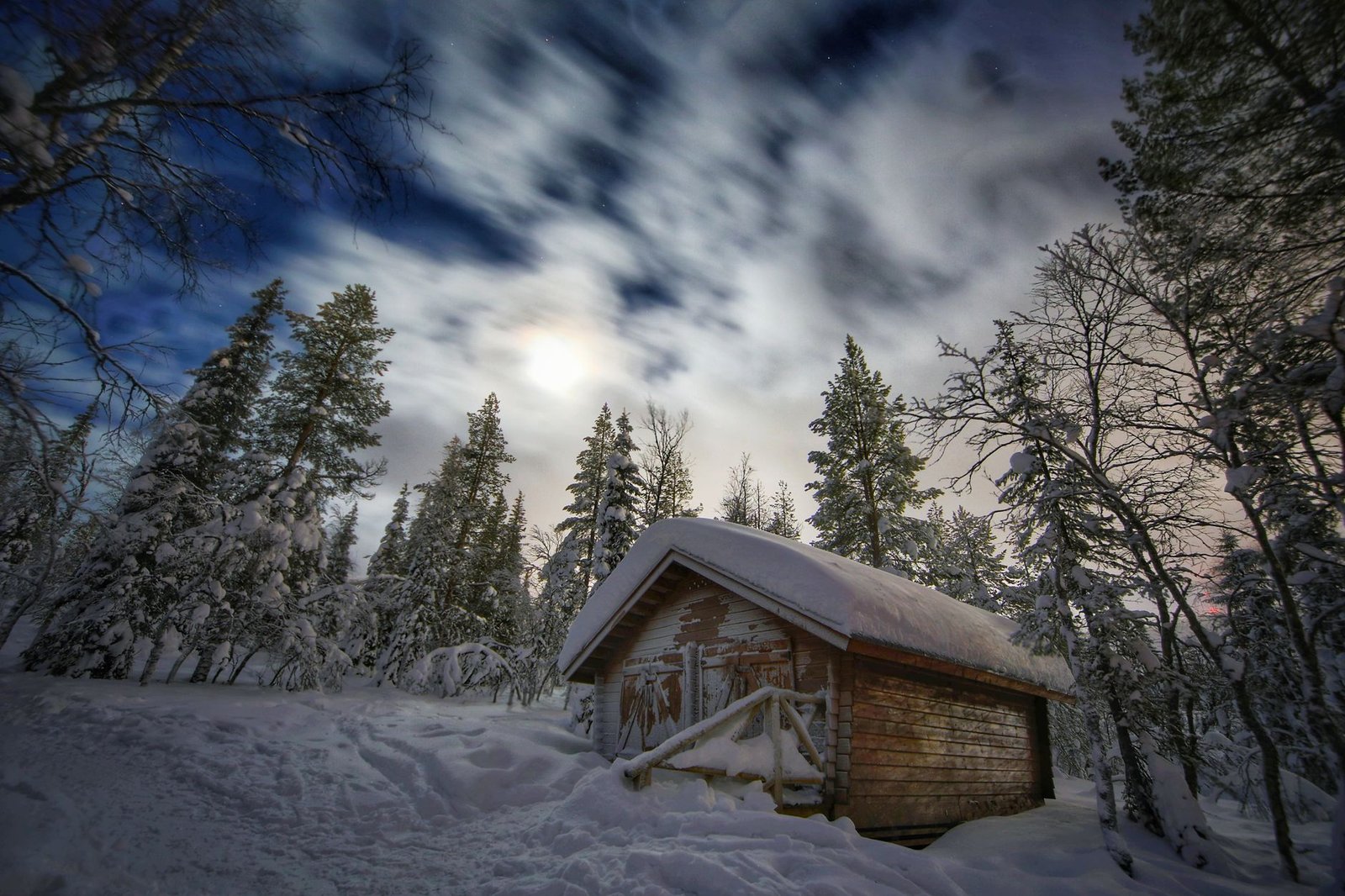 Lämmin mökki Inarissa kaamosaikaan, ikkunasta näkyy luminen metsä