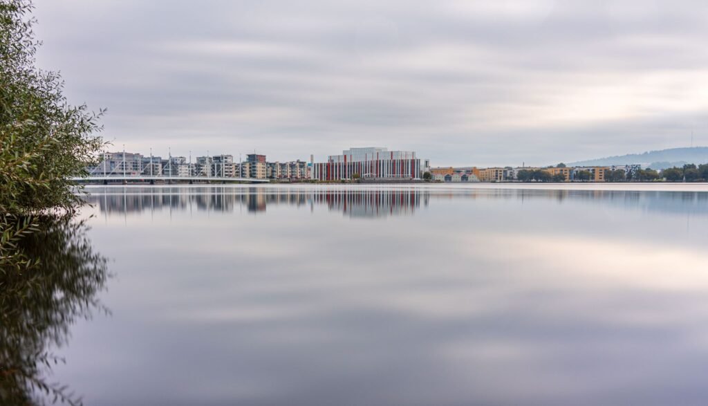 Rauhallinen heijastus Jönköpingin kaupunkimaisemasta tyynellä järvellä, joka esittelee modernia arkkitehtuuria.